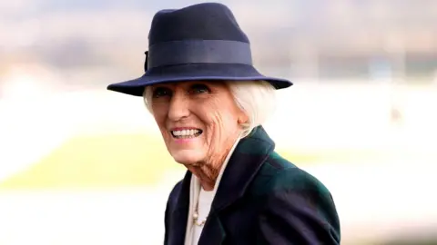 PA Media Mary Berry wearing a dark blue and green jacket, a dark blue sun hat and a white top. She has short white hair and smiles at the camera.