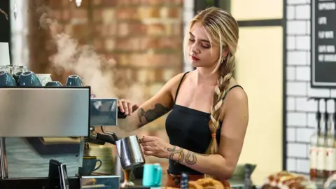 Getty Images A young female worker uses a coffee machine in a shop.