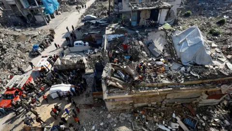 Reuters People watch a search and rescue operation at the site of a house that collapsed in Shati refugee camp, north-west of Gaza City (16 December 2025)