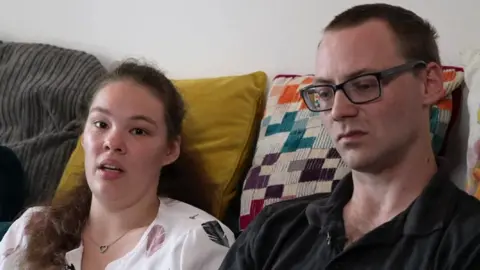 Couple affected by high rental costs who were forced to move to a smaller house sitting on a sofa