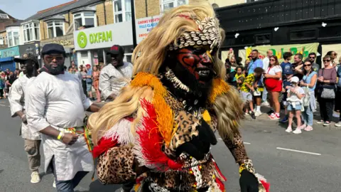 A man wearing leopard print dress with his face painted red black and yellow.