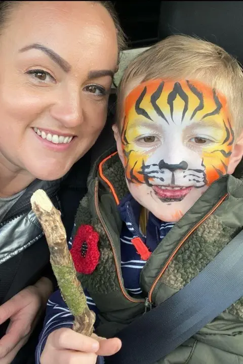 Samantha Evans-Browning A woman and a little boy looking at the camera. The boys face is painted as a tiger and he is holding a stick.