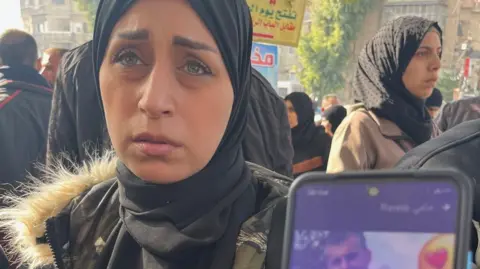 A woman in Damascus holds up her phone showing a photo of the relative she's looking for