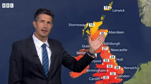 Weather presenter standing in front of a map with a lot of red across the map 