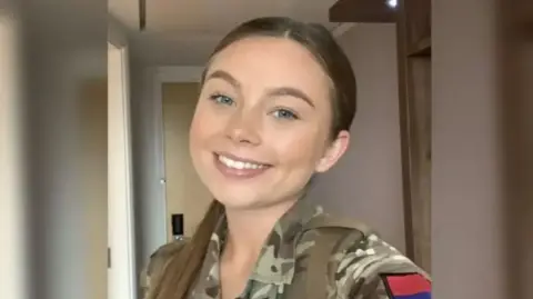 Jaysley Beck smiles at the camera in her camouflage army uniform. She has her brown hair tied back in a ponytail