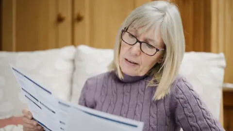 Woman looks at a bill while sitting on a bed