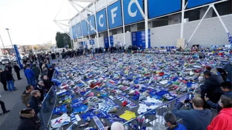 Reuters Rows of flowers and blue Leicester City shirts and flags laid out in front of a football stadium.