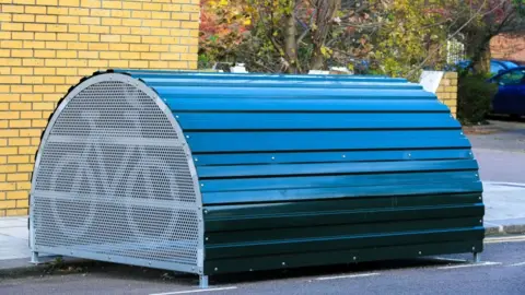 A bike hangar on a street, blue with a metal door with a bike symbol