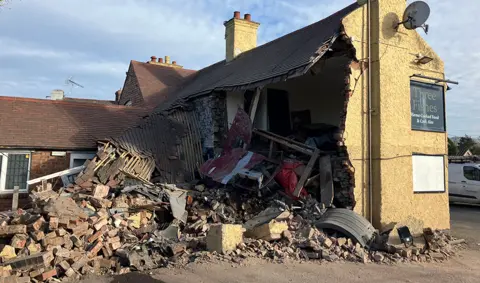 A damaged beige-coloured building with large chunks taken out of the sides and bricks exposed.  