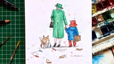 A drawing of the back of Queen Elizabeth II, dressed in a green coat, a green hat and brown shoes, holding a brown bag. She is walking hand in hand with Paddington Bear, wearing a blue coat, a red hat and red wellies, carrying a brown suitcase. A corgi is also walking next to Queen Elizabeth II, with red white and blue bunting draped over it. It is sketched on a white piece of paper and laid on art equipment, including paints and pain brushes.