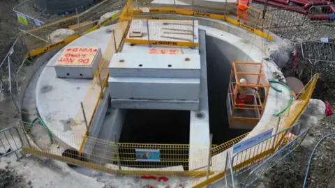 A concrete tank buried in the ground surrounded by building materials. The tank isn't operating yet but will contain 300,000 litres of waste water.
