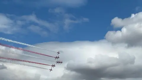 Red Arrows flying in formation, with red and white smoke trailing behind
