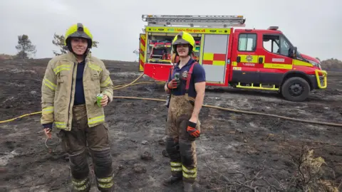 Leicestershire Fire and Rescue Service Two firemen pictured with a Variable Response Vehicle during a deployment to Dorset last year. The ground is burnt extensively around them. 
