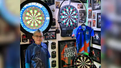 Gary Wharf Lennon Wharf surrounded by darts merchandise, including three boards