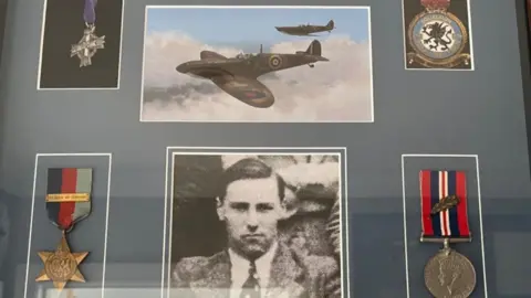 Kent Battle of Britain Museum Trust A collection of World War Two medals and photos behind a window cabinet.