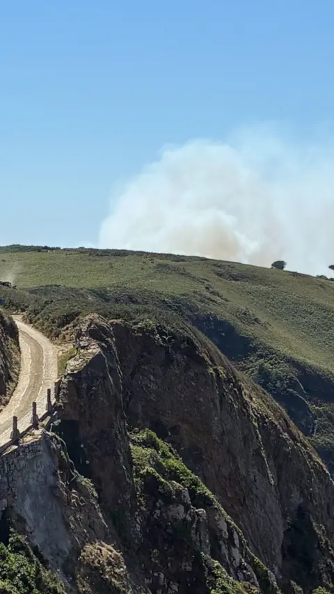 White smoke rising from green headland