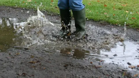 BBC A picture of a child wearing wellies jumping into a muddy puddy. The wellies are dark green in colour.