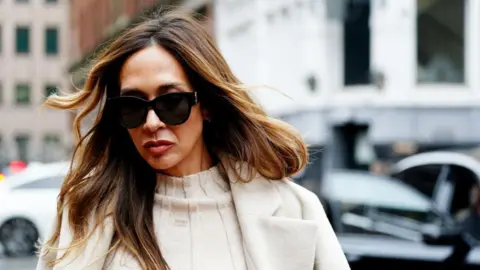 PA Media A woman with long brown hair is pictured wearing a cream-coloured coat and sunglasses.