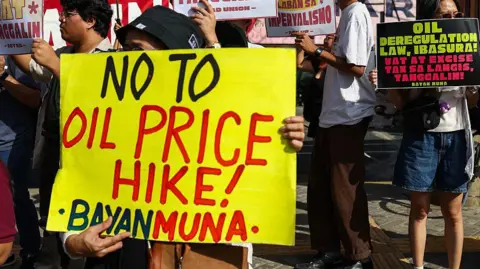 Getty Images Protesters gather for a rally at a bus station in the Philippines, with one holding a sign saying "No to Oil Price Hike!"