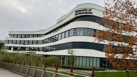 A four -storey modern white winding building with James Grant/BBC "University of northampton" Sign the top.