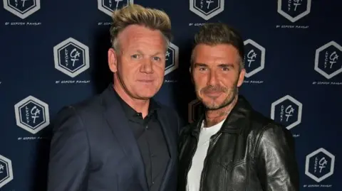 Getty Images Gordon Ramsey in a navy blue suit and black shirt, with David Beckham in a black leader jacket and white t-shirt.