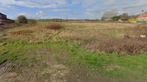 Open green land between two sets of developments.