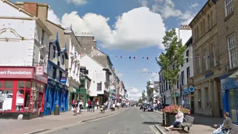 Google Photo of Stricklandgate in Kendal, showing various shops and street furniture