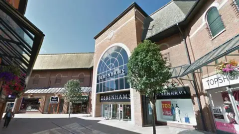 The Debenhams store is a multi-storey brick building. It has a grand arch window with a sign reading "Debenhams" on it.