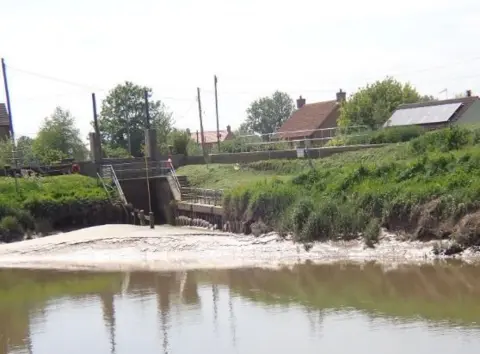 Ivan Cane The River Great Ouse at Salters Lode in Norfolk, showing silt levels above the water line at the river bank and the entrance to the lock, which goes under a road bridge.