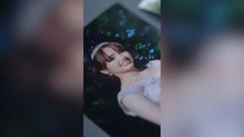 A young woman with dark red hair pulled away from her face wears a pink formal dress