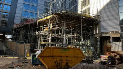 A yellow skip and scaffolding outside the hotel.