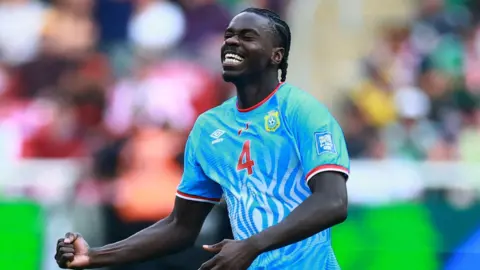 DR Congo defender Axel Tuanzebe celebrates a goal for his country against Jamaica in their World Cup play-off win. He is seen from waist up clenching his right fist at waist level while tilting his head up slightly, with eyes closed and a look of delight on his face