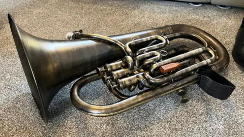 The image shows the antiqued brass euphonium resting on some grey carpet.