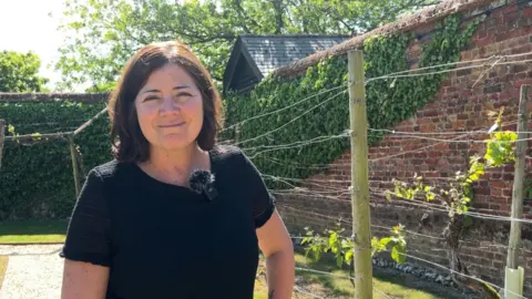BBC A woman stood in a vineyard smiling into the camera