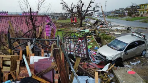 Reuters/Raquel Cunha A house which has been destroyed in the hurricane, plus a car which has been damaged, and a road littered with debris. 