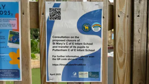 A notice on a fence which says "Consultation on the proposed closure of St Mary's C of Infant School and transfer of its pupils to Puttenham C of E Infant School."