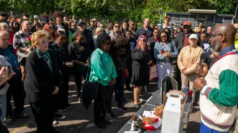 PA Media Members of the community standing around. Some hold a candle and others wipe tears from their eyes.