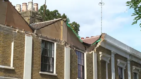Damage to the upper frontage and roofline of terraced houses on Woodland Terrace in Charlton. Sections of brickwork and masonry have fallen away, exposing parts of the structure beneath the roof