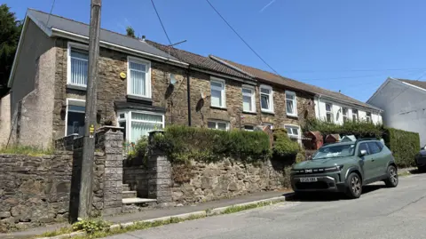Local Democracy Reporting Service A row of terraced stone houses in Pontycymer. A green car is parked outside the front of one of the houses. A stone wall runs in front of the properties. 
