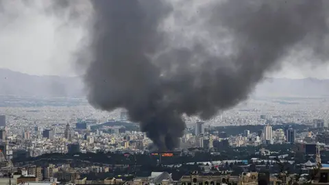 Smoke rises from Iranian TV building as part of wide shot of city of Tehran