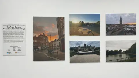 Martin Phillips/Historic England A caption board showing the work is from The Royal School, Wolverhampton, alongside five enlarged photos: a sunset cityscape, a football painted on tarmac, a rooftop view of a spire, a historic house and a stretch of water behind railings.