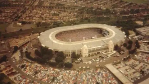 Kevin Armstrong at Wembley Stadium on July 13, 1985, the morning of Live Aid. The stadium is full, hundreds of cars parked outside.