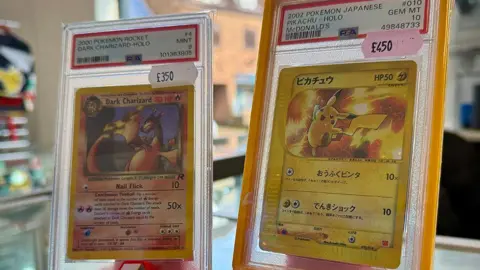 Two Pokémon cards in clear plastic cases on sale in a shop.