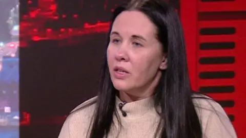 BBC Sharon with long dark hair wearing a cream jumper in the BBC North West Tonight studio.