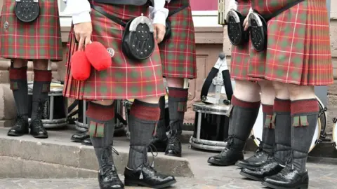 Getty Images Five men in red and green kilts, photographed from the waist down. They are wearing full traditional outfit, with sporrans and shoes laced around their calves. 