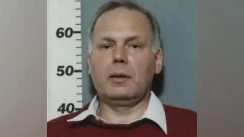 Police handout A police mugshot of a man with short greying hair wearing a red jumper with a white collar popping out