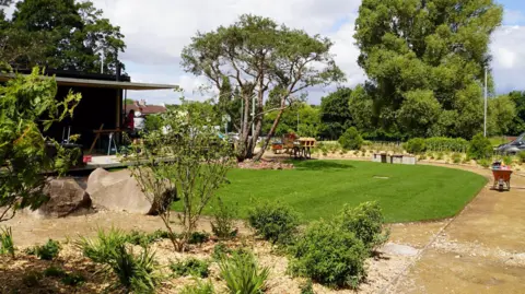 Simon Thake A plush garden with immaculate green grass surrounded by neat shrubs and tall trees