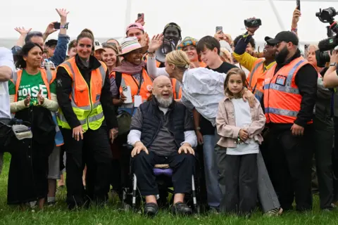 Emily and Michael Eavis smile in front of a crowd of volunteers and festival staff as the gates are opened. 