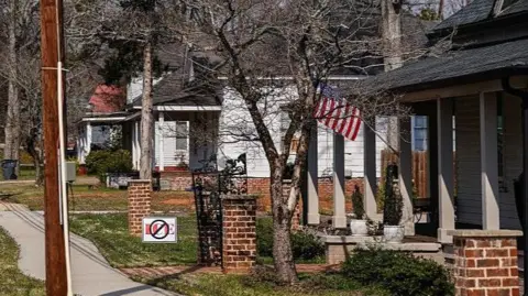Getty Images A view down a street in Social Circle, with small homes on one side and a white church spire in the distance. On one lawn is a sign that says ICE - crossed out