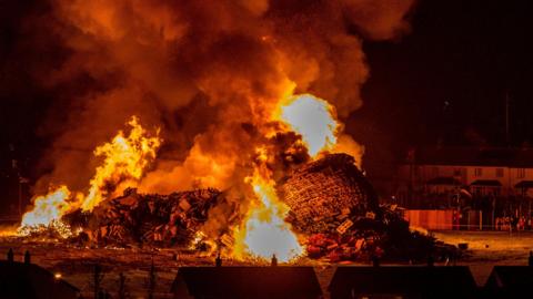 A burnt bonfire, large flames and pallets fallen over 